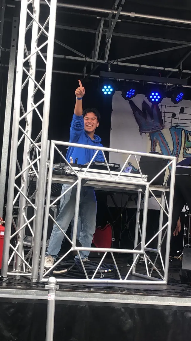 Tjinnakon wijst enthousiast naar het publiek tijdens een optreden op een buitenpodium.